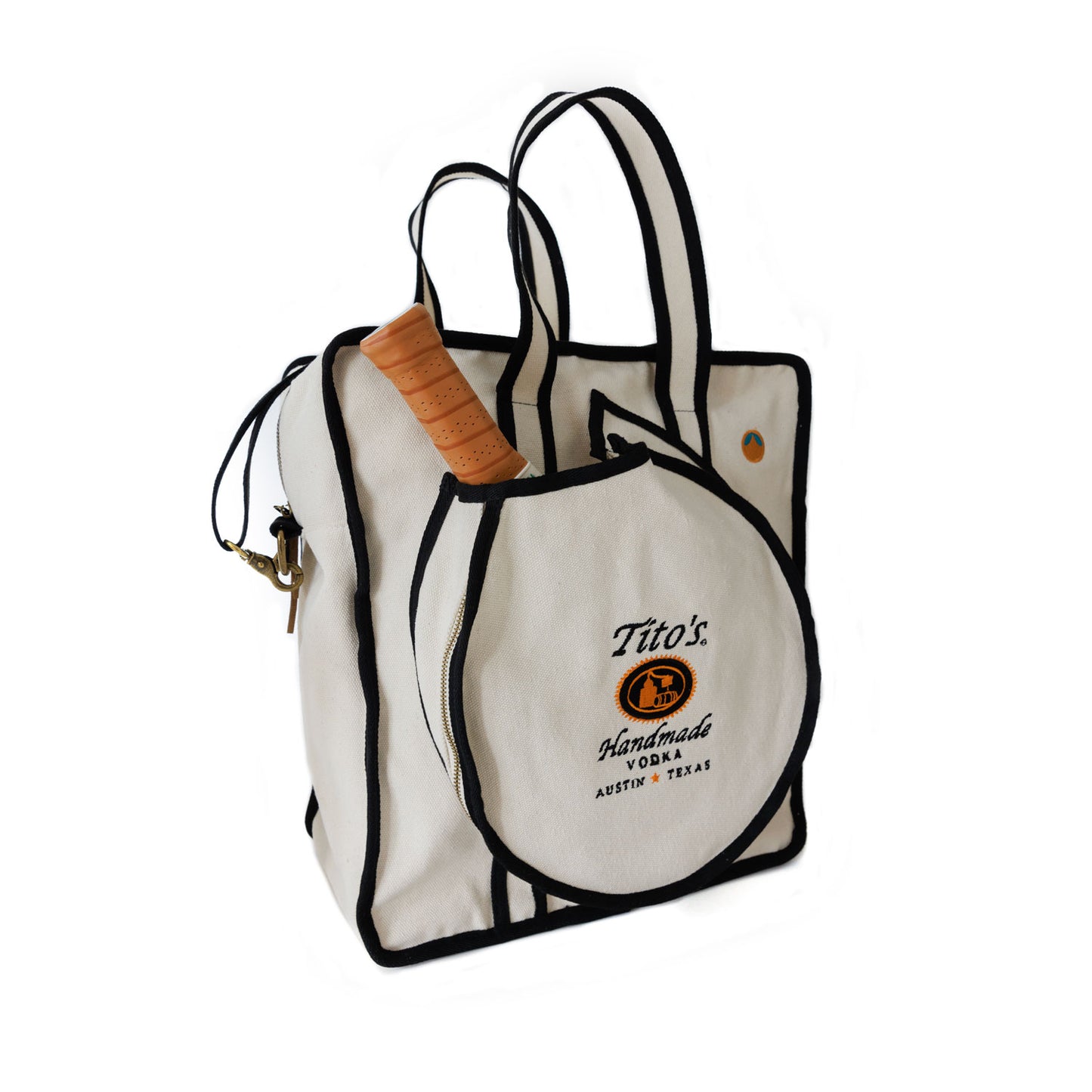 Front of cream color Tito's X Tangerine Pickleball Bag with black trim, Tito's Handmade Vodka logo, adjustable strap, and paddle pocket