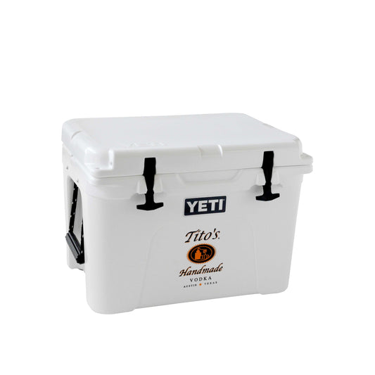 Front view of white YETI hard cooler with black and orange Tito's Handmade Vodka logo and black handles