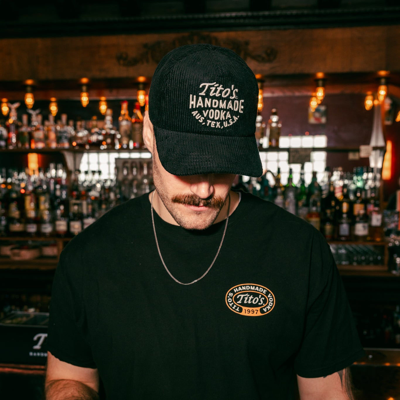 person wearing Tito's Corduroy hat and Tito's Martini Tee in a bar