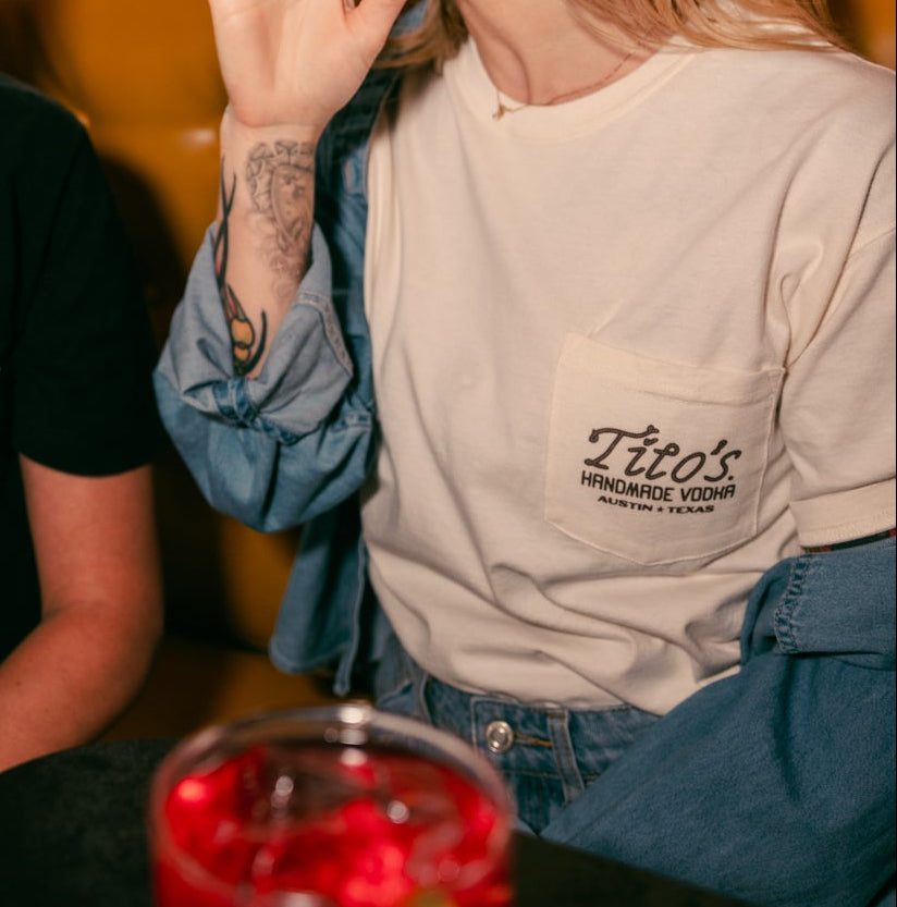 Person sitting at a table with a Tito's cocktail wearing a Tito's Rodeo Tee