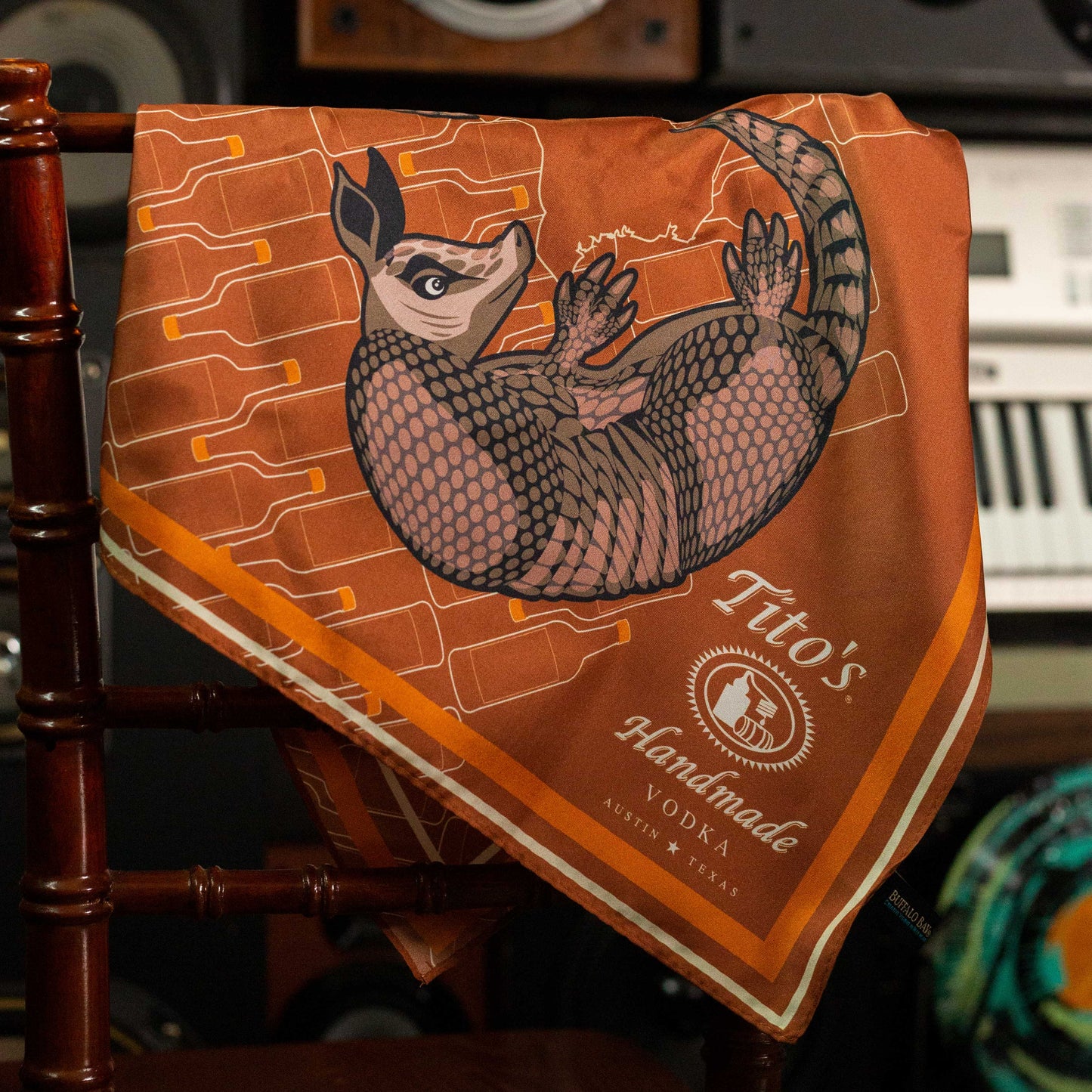 Copper silk scarf featuring white Tito's Handmade Vodka logo with illustrated armadillo and bottle designs