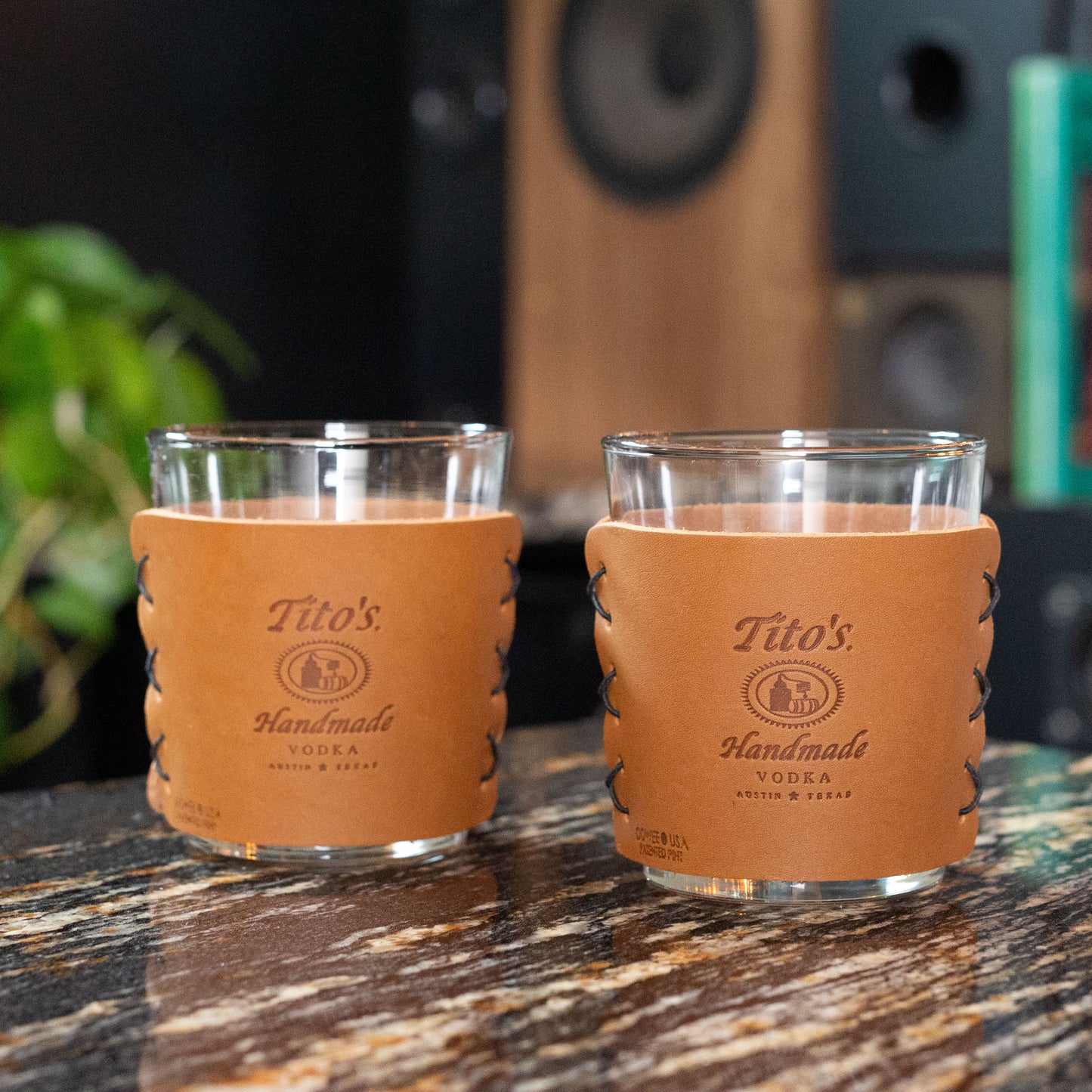 Detail view of highball cocktail glasses in leather sleeves with Tito’s Handmade Vodka logo and black stitching on a table