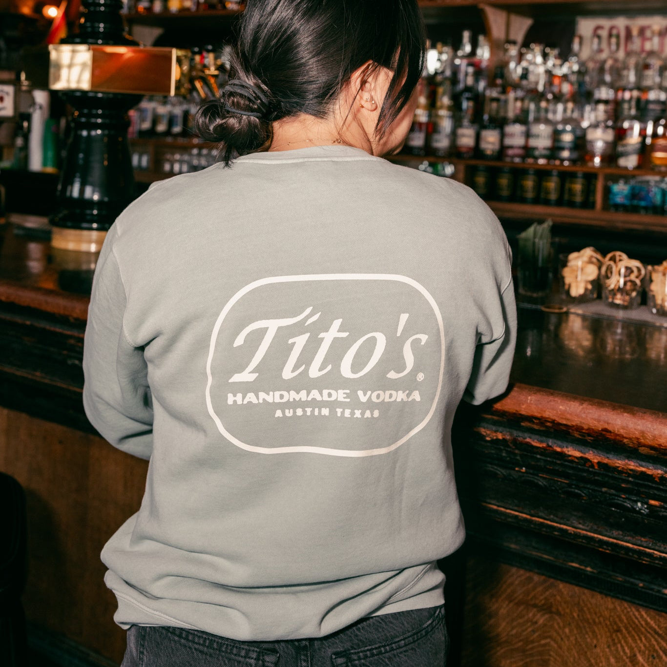 back view of a person wearing the Tito's Austin Crewneck at a bar 