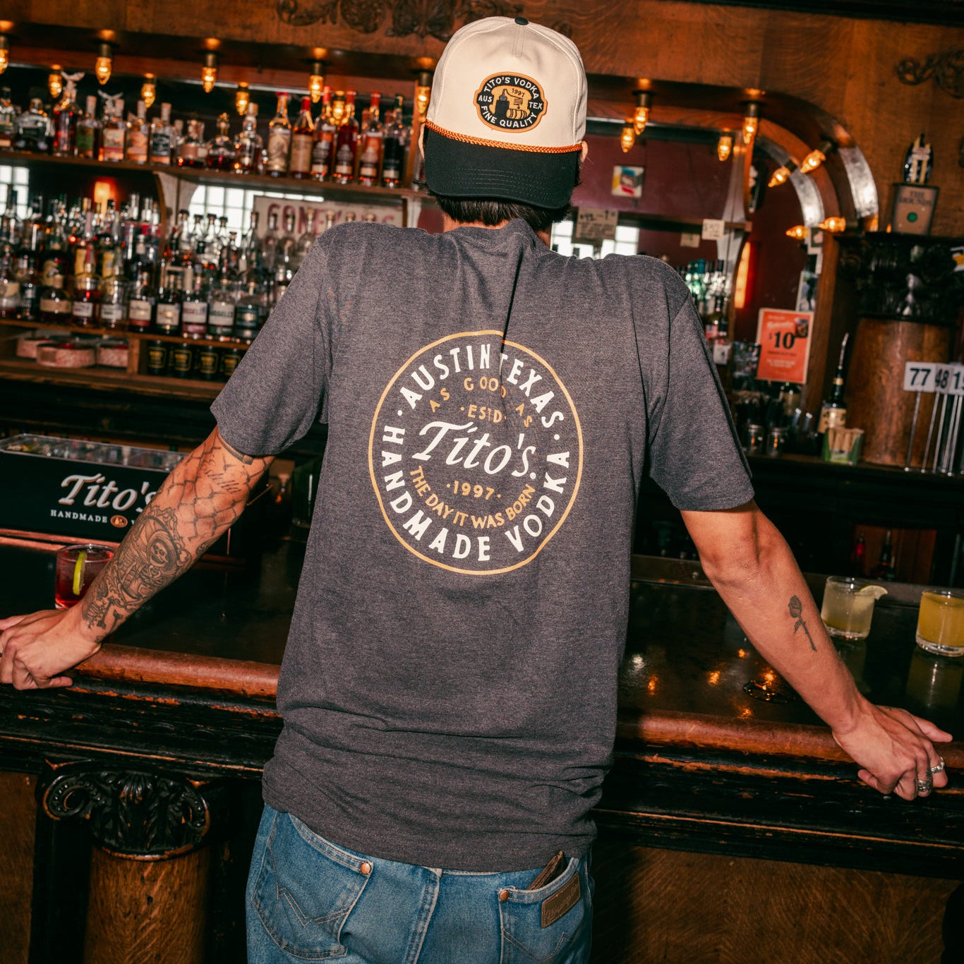 back view of a person wearing the Tito's Austin Tee and Tito's Texas Patch Hat at a bar 
