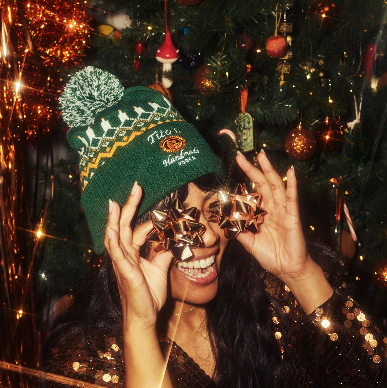 Person wearing the Tito's Ugly Beanie with bows over their eyes in front of a Christmas tree