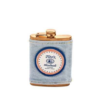 Front view of a copper flask with a demin wrap and a red, white, and blue circle patch with the Tito's Handmade Vodka logo
