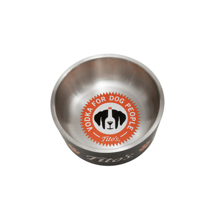 A stainless steel dog bowl with a black exterior, featuring a circular orange, white, and black logo on the inside that reads 'VODKA FOR DOG PEOPLE' and 'Tito's' . The brand name 'Tito's' is also visible on the outside of the bowl.