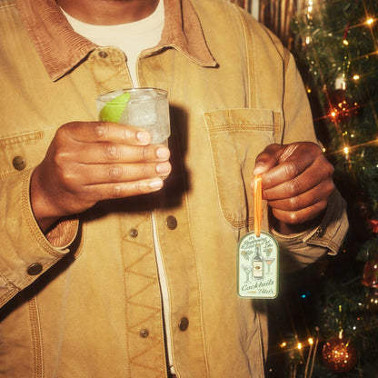 Person holding a Tito's Soda Lime cocktail in one hand and a Tito's Merry Martini Ornament in the other