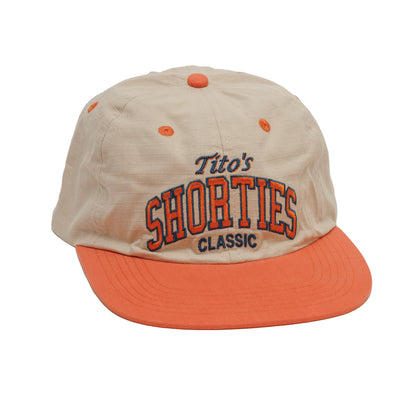 Front of Beige hat with orange bill and eyelets  with 'Tito's Shorties Classic' in navy and orange text