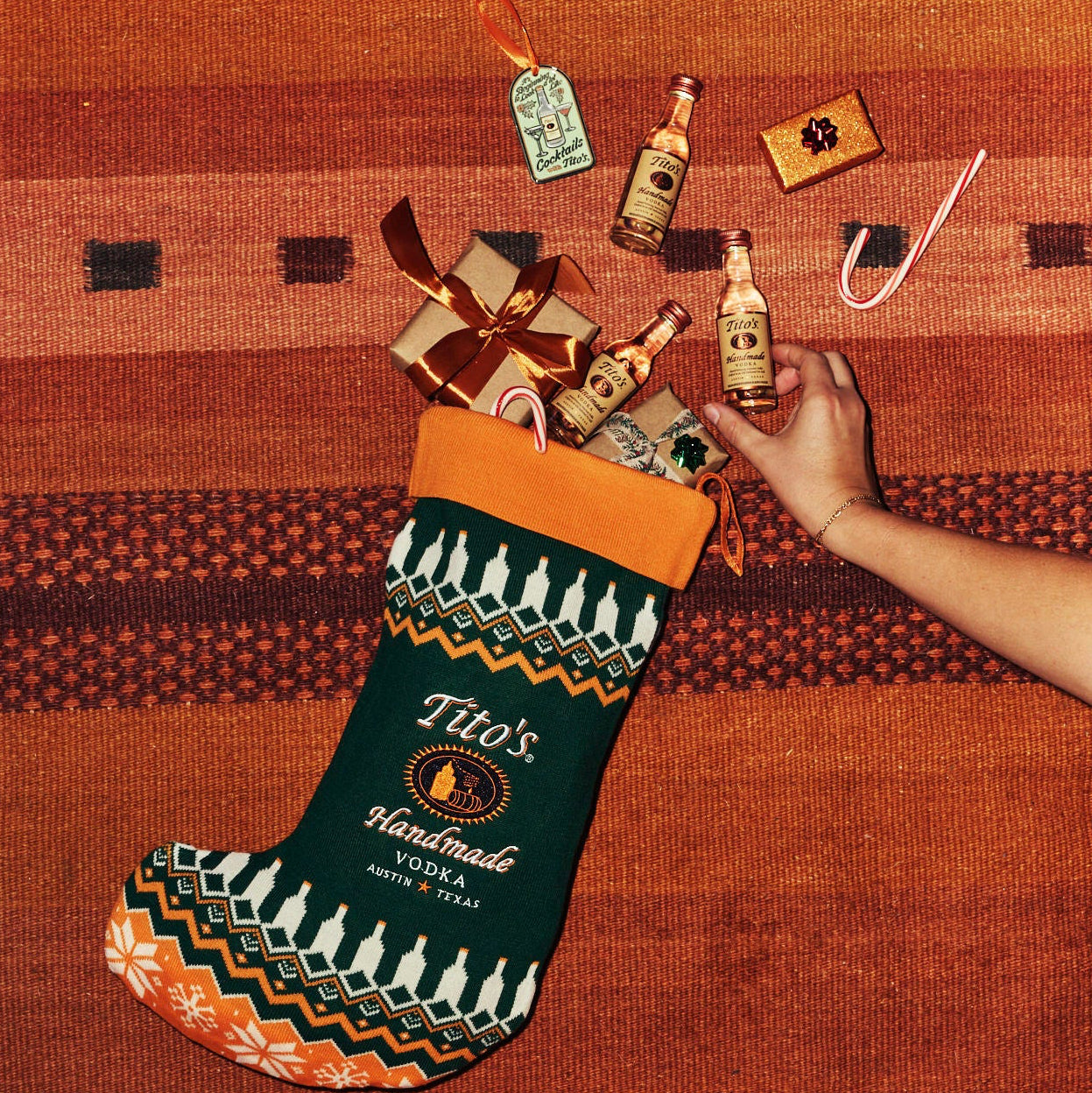 Person filling a Tito's Handmade Vodka stocking with bottles on a textured surface