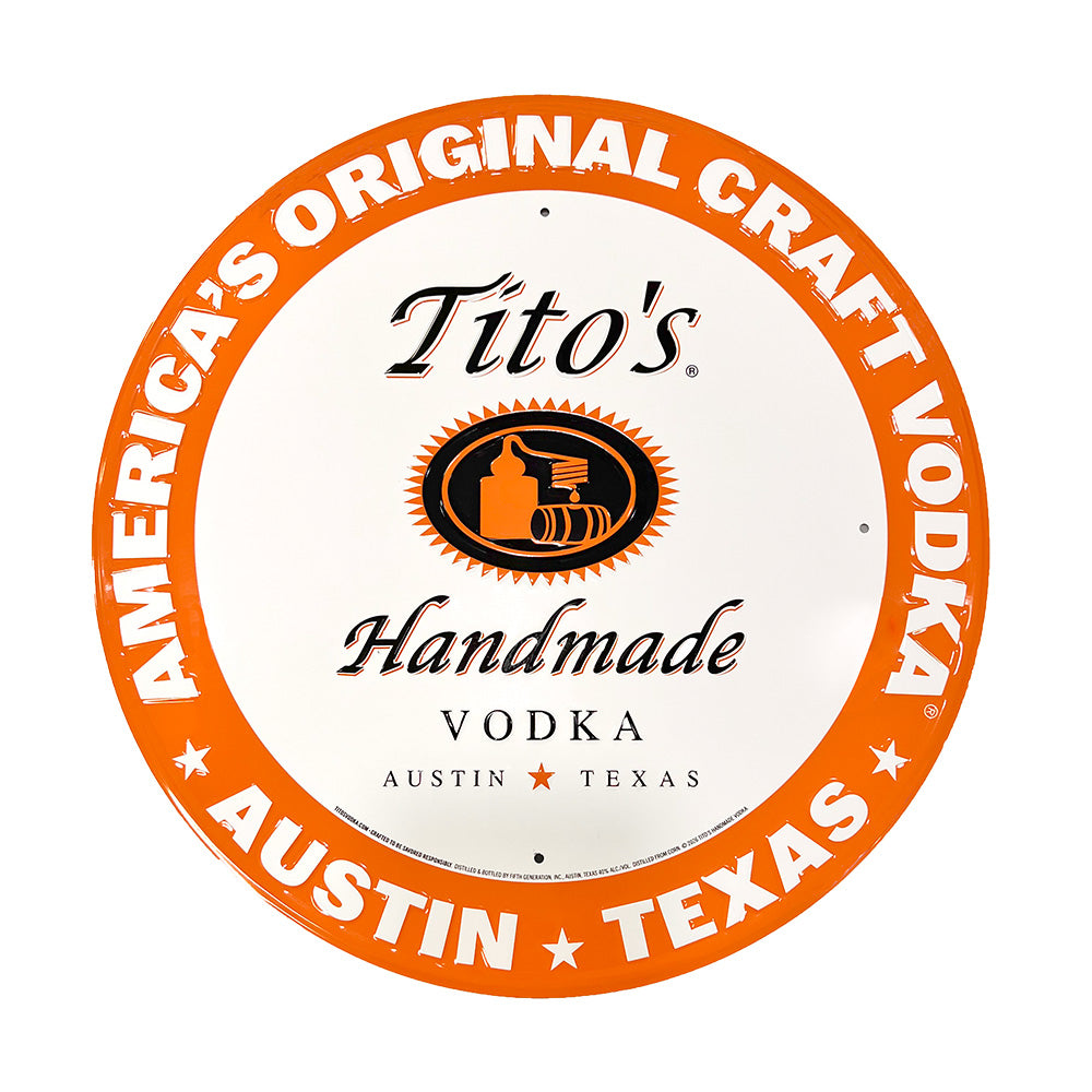 Round sign with white background and Tito's Handmade Vodka logo in the center with an orange boarder that says "America's Original Craft Vodka Austin, Texas"