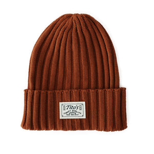 Front view of ribbed rust colored beanie with white patch on the cuff