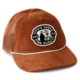 Front view of rust colored corduroy hat with mesh back. White rope across the brim with a black and white patch with words "Tito's Vodka Fine Quality" and potstill