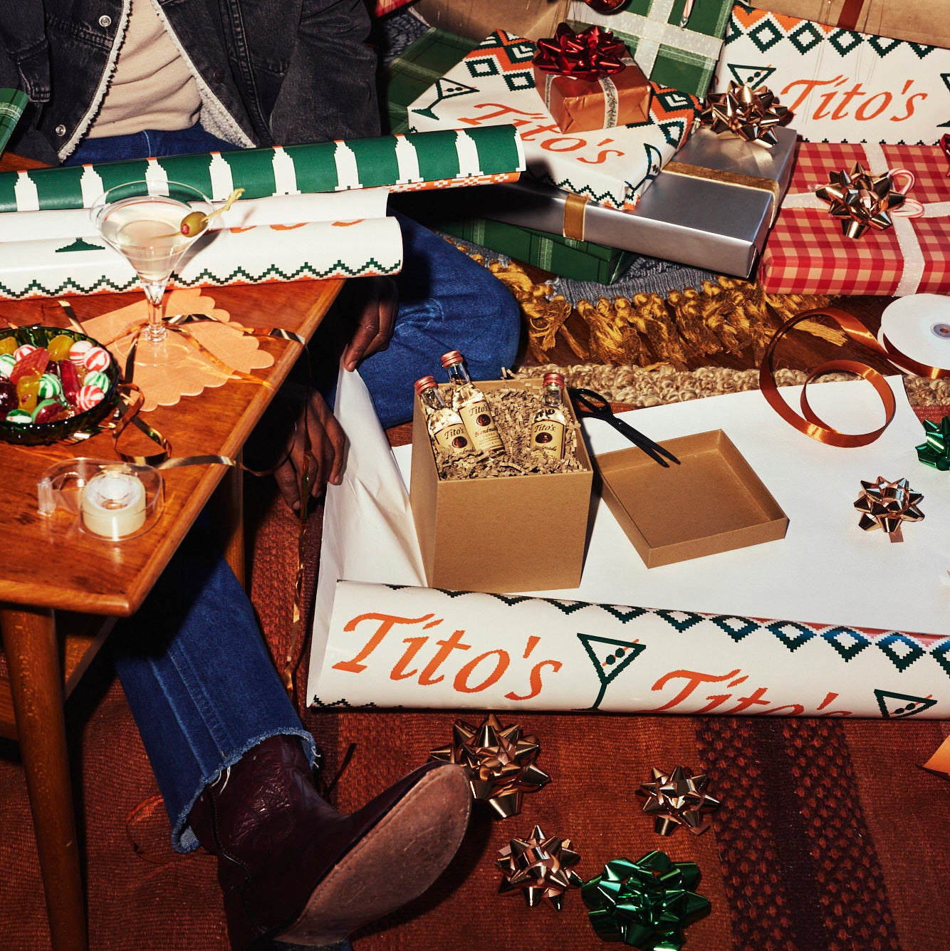 Person wrapping a box full of 50ml Tito's Handmade Vodka bottles in Tito's Ugly Wrapping Paper