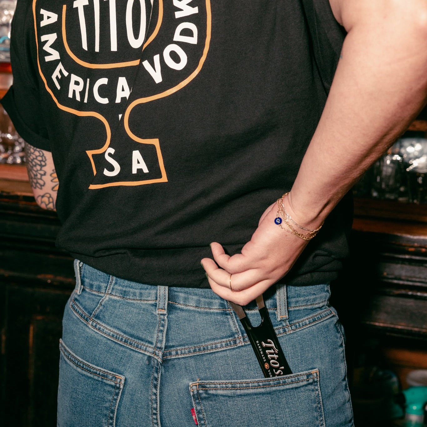 Person wearing a Tito's Martini Tee pulling a Tito's bar Key out of their back pocket