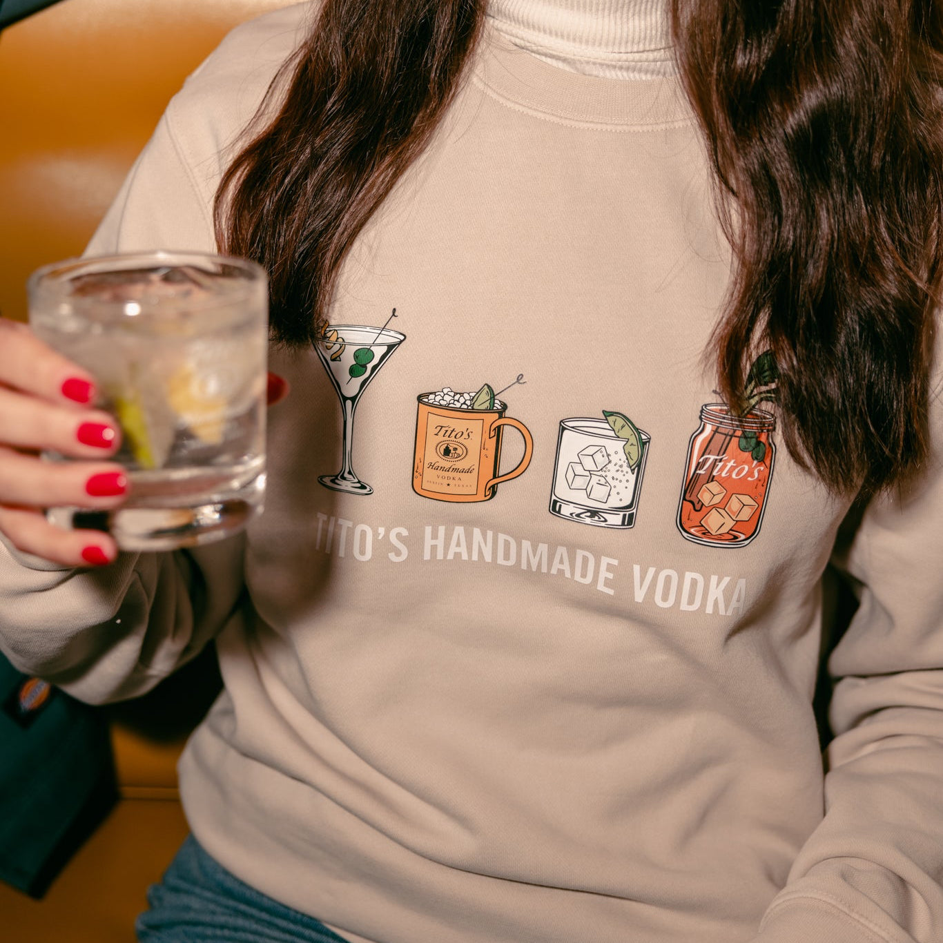 front view of a person wearing a Tito's Classic Cocktail crewneck holding a Tito's Soda Lime cocktail 