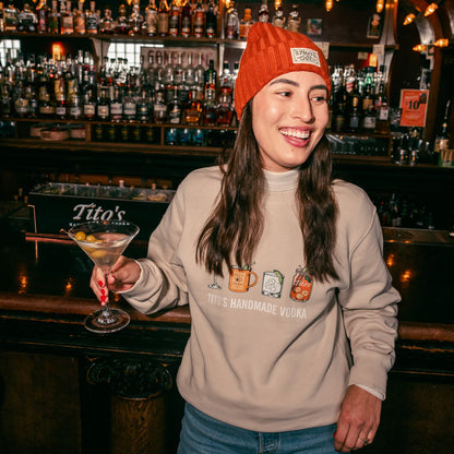 Person wearing a Tito's Copper Beanie and a Tito's Cocktail Sweater holding a Dirty Tito's Martini in a bar 