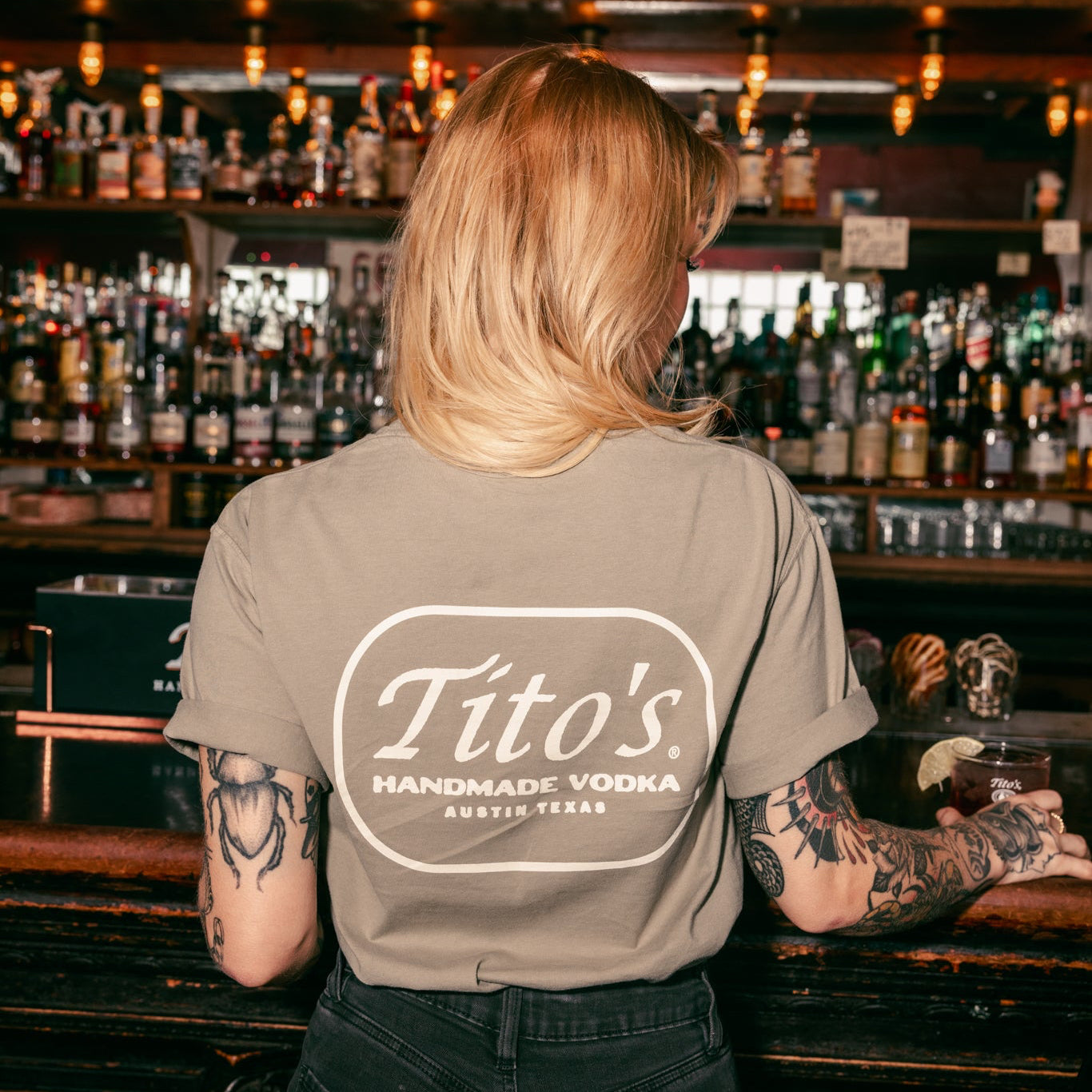 Back of person wearing a Tito's Hometown Tee in a bar setting