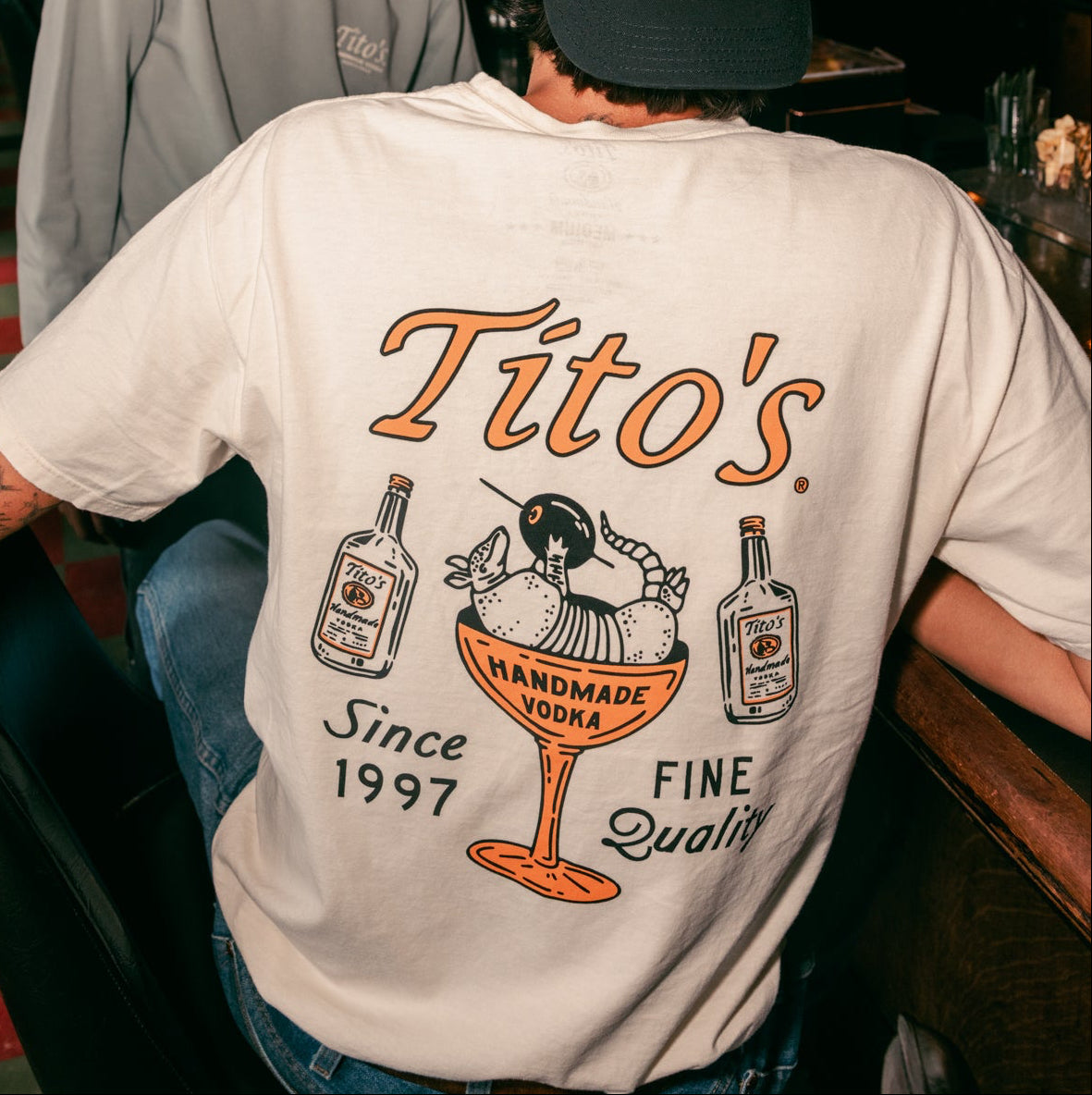Back view of a person wearing the Tito's Lounging Armadillo Tee at a bar 