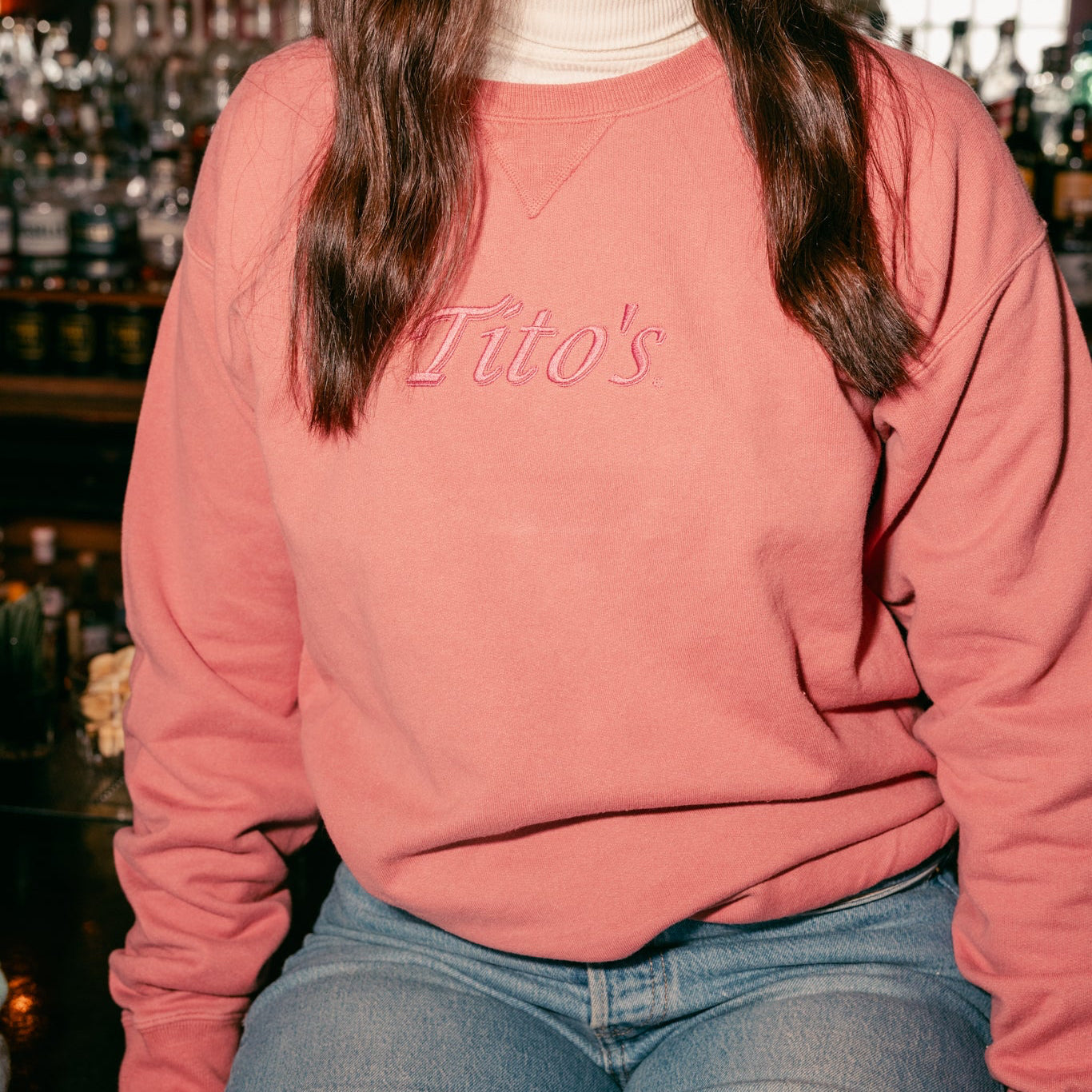 Person wearing the Rust colored Tito's Classic Crewneck sitting on a bar 