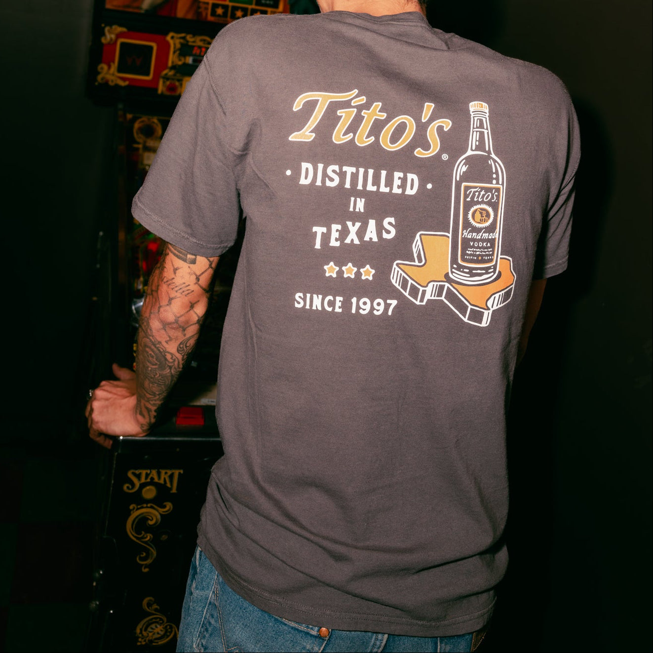 back view of a person wearing Spirit of Texas tee playing an arcade game 