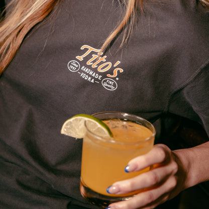 person wearing a Spirit of Texas Tee holding a Tito's cocktail