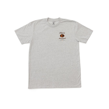 A light heather gray short-sleeve t-shirt with a Tito's Handmade Vodka logo on the left chest in black and orange. 