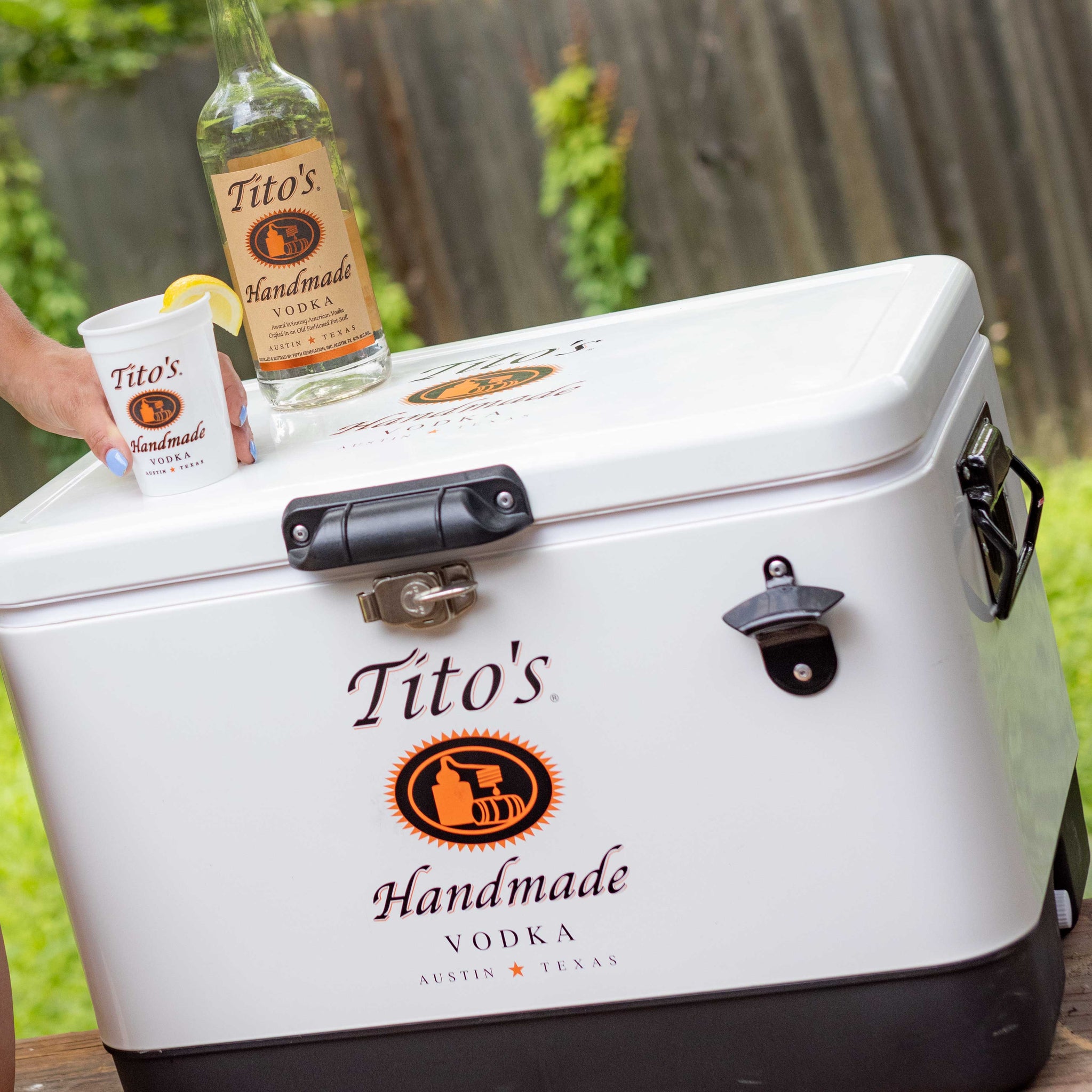 White cooler with stainless steel hardware accessories and bottle opener on front with Tito's Handmade Vodka Logo