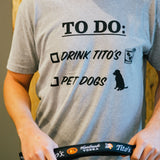 Person wearing gray short-sleeve t-shirt with To Do list, Drink Tito's, Pet Dogs on front and holding a Tito's Dog Leash