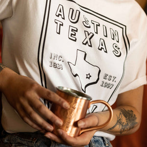 Girl wearing Tito's Hometown Hero Tee and holding a cocktail in a Tito's copper mug