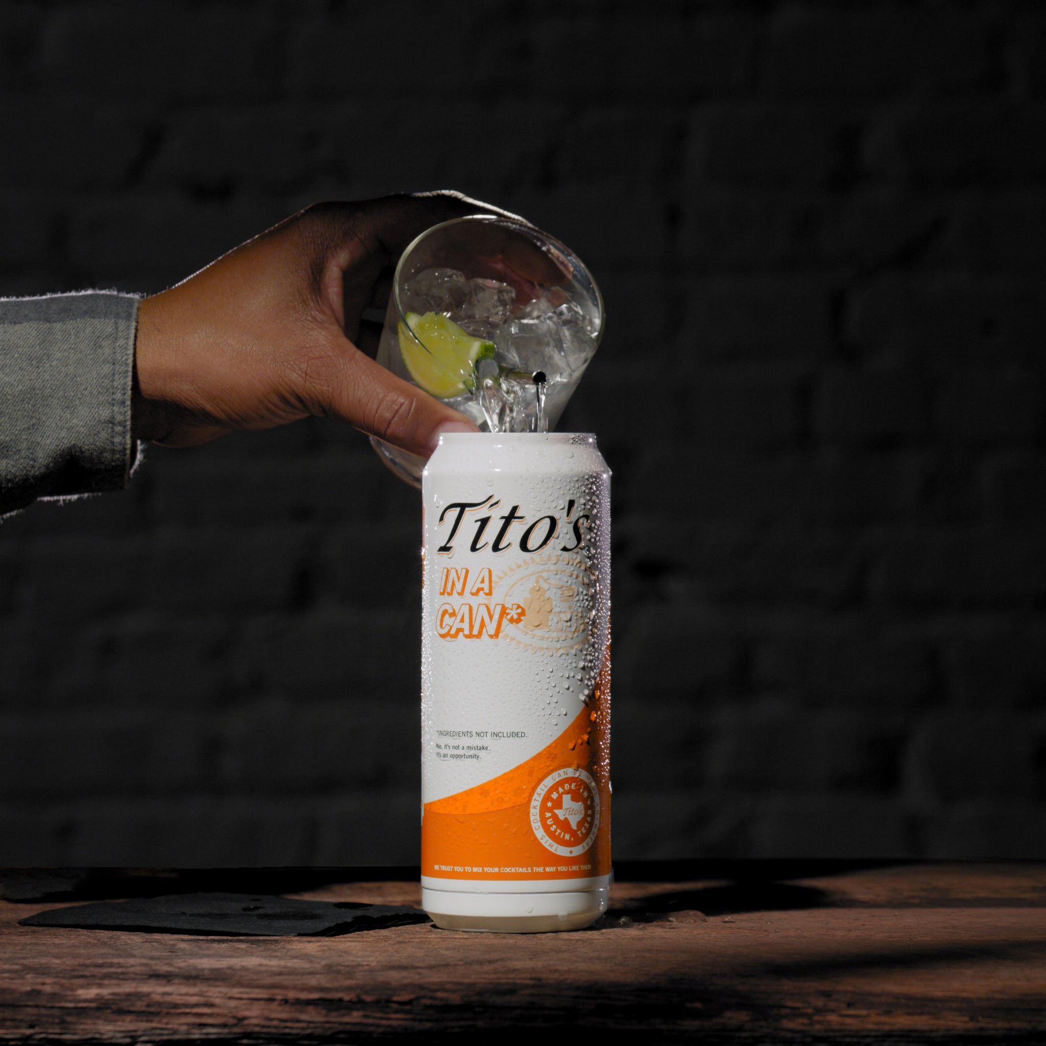 Hand pouring cocktail into orange and white stainless steel Tito's in a Can* tumbler