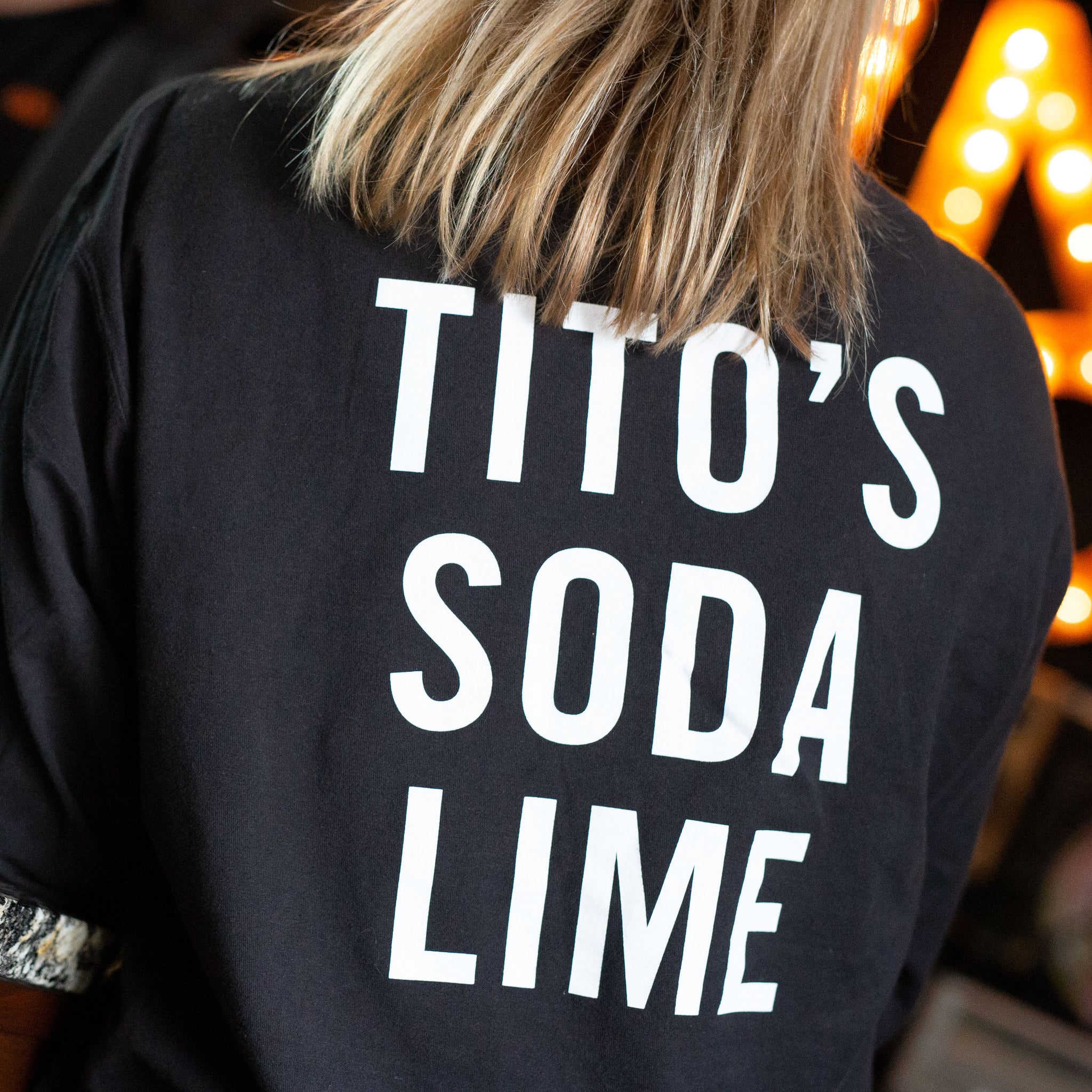 Woman wearing black long-sleeved t-shirt with Tito's Soda Lime