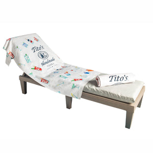 White towel with Tito's Handmade Vodka logo and assorted cocktail illustrations on a chaise lounge chair.