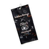Black golf towel with Tito's Handmade Vodka X William Murray logo, golf and cocktail illustrations, and silver metal carabiner 
