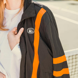 Woman wearing black track jacket with pot still design on left chest